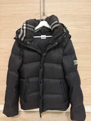 Burberry jacka/väst - Säljer en svart pufferjacka från Burberry med avtagbara ärmar så den kan användas som väst. Kommer med tags. Storlek L men passar även M.