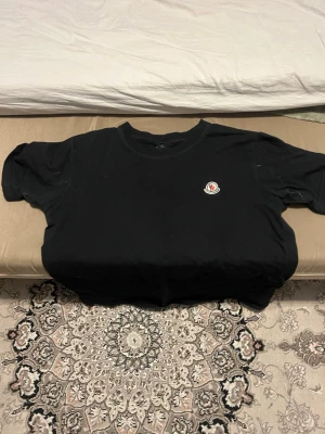 Svart Moncler t-shirt med logga - Snygg svart t-shirt från Moncler med klassisk rund hals och korta ärmar. På bröstet sitter Monclers ikoniska logga i vitt, rött och blått. Tillverkad i mjuk bomull som känns skön mot huden. Perfekt för dig som gillar stilrena plagg med exklusiv känsla.