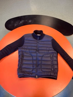 Moncler Cardigan Mörkblå - Mörkblå cardiganjacka med quiltad framsida och ärmar i mjukt tyg. Jackan har ståkrage, två dragkedjefickor fram och ribbade muddar. Perfekt för lager-på-lager och en stilren look. För fler frågor kom privat!