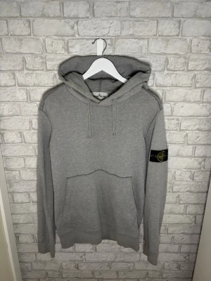 Stone Island hoodie - Stone Island hoodie i grå färg. Clean och populär modell med badge på armen. Finns några svaga missfärgningar/slitage vid luvan och baktill, inget som syns tydligt vid användning.