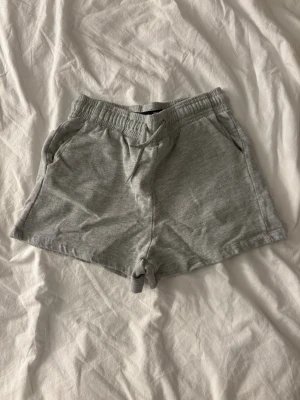 Grå mjukisshorts med snörning XS - Gråa mjukisshorts från 157 i storlek XS. De har elastisk midja med snörning och två sidofickor. Perfekta för chill dagar eller när du vill vara bekväm. Klassisk och enkel design i mjukt bomullsmaterial.