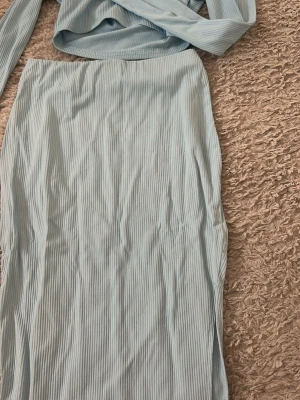 Ljusblå ribbad långkjol - Säljer en ljusblå långkjol med ribbad struktur och slits på sidan. Kjolen har en enkel och stilren design som passar perfekt till både vardags- och trendiga outfits. Materialet känns mjukt och följsamt mot kroppen.