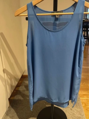 Blå ärmlös topp - Snygg blå topp med rund halsringning och enkel, stilren design. Toppen är ärmlös och har en lätt, flowy passform som känns luftig och bekväm. Perfekt att matcha med jeans eller shorts för en cool look.