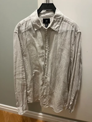 Ljusbeige linneskjorta från H&M - Säljer en ljusbeige skjorta från H&M i regular fit. Skjortan är tillverkad i linne, har klassisk krage, långa ärmar och knäppning framtill. Perfekt för en avslappnad men stilren look. Fint skick på den, hör av er om ni har frågor!