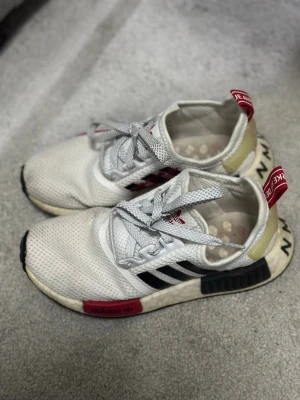 Adidas NMD R1 vita och svarta sneakers - Säljer ett par Adidas NMD R1 sneakers i vitt meshmaterial med svarta ränder och röda detaljer. 