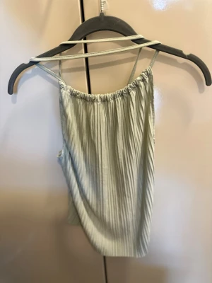 Ljusgrön plisserad linnetopp - Superfin ljusgrön linnetopp med tunna axelband och plisserat tyg. Toppen har en lös passform och är perfekt för varma dagar. Snygg att styla med jeans eller kjol för en chill look.