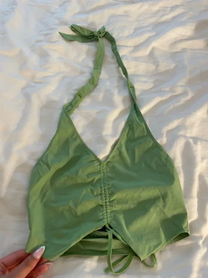 Grön bikiniöverdel med knyt - Snygg grön bikiniöverdel med halterneck och knyt i nacken. Toppen har en rynkad detalj framtill och justerbara band under bysten för perfekt passform. Perfekt för lata dagar på stranden eller poolen.