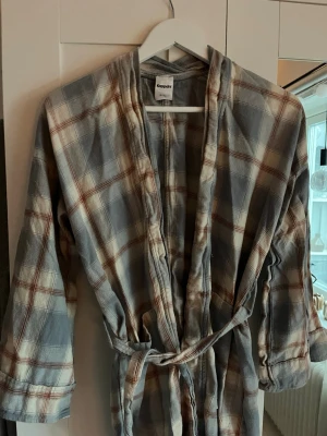 Rutigt pyjamas-set från Kappahl - Mysigt pyjamas-set från Kappahl i mjuk bomull. Setet består av en långärmad morgonrock med knytskärp och matchande byxor. Färgen är gråblå med rutigt mönster i vitt och brunt. Använder inte längre så säljer🩵 storlek s/m