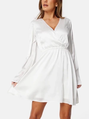 Vit skolavslutnings klänning satin - Snygg vit omlottklänning i satin med långa ärmar och markerad midja. Klänningen har en elegant v-ringning och ett mjukt, glansigt material som ger en lyxig känsla. Perfekt för dig som gillar stilrena och trendiga plagg.