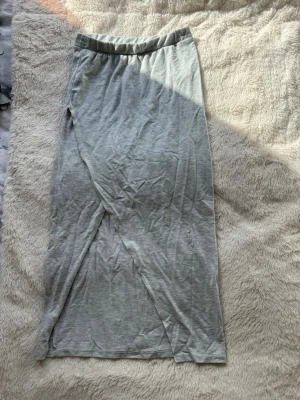 Ljusgrå långkjol med omlott - En enkel och stilren ljusgrå långkjol i mjukt material. Kjolen har en omlott-design framtill och resår i midjan för extra komfort. Perfekt att styla med sneakers eller sandaler för en avslappnad look.