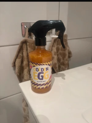Golden Egg Glitter Mist från Lush - Golden Egg Glitter Mist från Lush är en ansiktsspray med guldigt skimmer. Flaskan är genomskinlig med svart spraymunstycke och etikett i gult, lila och vitt. Perfekt för dig som vill ha extra glow och glitter i din look.