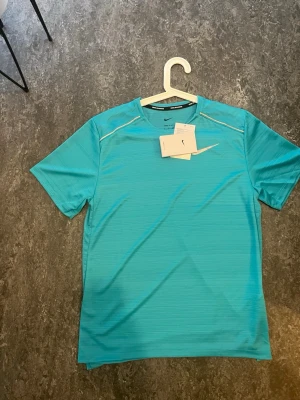 Nike running Turkos  - Snygg turkos tröja från Nike med rund hals och diskreta reflexdetaljer på axlarna. Tröjan har Nike-logga i silver på bröstet och är tillverkad i ett lätt, snabbtorkande material som passar perfekt för träning och löpning eller bara chilla 
