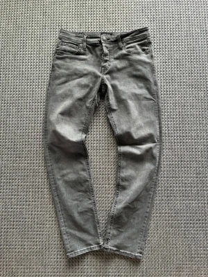 Grå slim fit jeans från Jack&Jones - Säljer ett par grå slim fit jeans med klassisk femficksdesign och normalhög midja. Jeansen har raka ben och är tillverkade i ett mjukt denimtyg som ger en skön känsla. Passar perfekt till en avslappnad grisch look. 