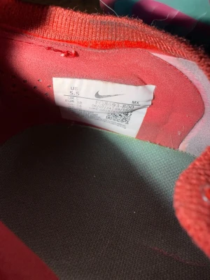 Nike Mercurial elite AG röda fotbollsskor - Säljer ett par Nike Mercurial fotbollsskor i en snygg rosa färg med gröna detaljer under sulan. Skorna har fasta dobbar och är designade för bra grepp på planen. Lätta och smidiga med klassisk snörning, perfekta för dig som vill ha snabbhet och kontroll.