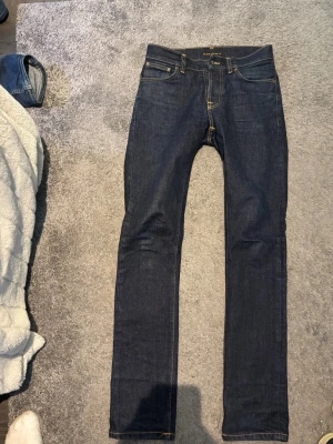 Mörkblå smala jeans från Nudie Jeans - Snygga mörkblå jeans från Nudie Jeans i klassisk slim fit-modell. Jeansen har fem fickor, kontrastsömmar och är tillverkade i kraftig denim. Perfekta för dig som gillar en stilren och tidlös look. L34