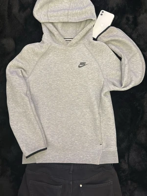 Grå Nike hoodie med huva - Säljer en stilren grå hoodie från Nike med klassisk logga på bröstet. Hoodien har en mjuk och skön känsla, raglanärmar och en stor huva. Perfekt för dig som gillar sportig och avslappnad look. Materialet är bomullsblandning.