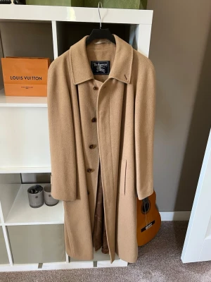 Burberry Kappa - En Klassikt vintage kappa från burberry från tidigt 90-tal , i 100% viskos vilket är ett unikt och miljövänligt material.