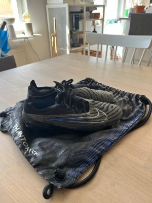 Nike Phantom GX fotbollsskor svart/grå - Säljer ett par Nike Phantom GX fotbollsskor i svart och grått med blå detaljer. Levereras med originalpåse. Stl 40