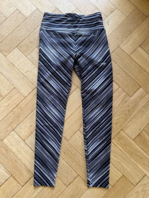 Svarta mönstrade träningstights - Snygga svarta träningstights från Röhnisch med diagonalt randigt mönster i vitt och grått. Hög midja och stretchigt material som sitter skönt på kroppen. Perfekta för gymmet eller löprundan.