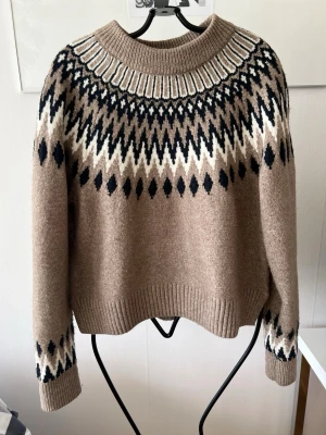 Beige stickad tröja från H&M XS - Stickad tröja från H&M i beige med svart och vitt nordiskt mönster runt halsen och på ärmarna. Tröjan har ribbstickad krage, ärmslut och nederkant. Perfekt för kalla dagar och riktigt snygg till jeans.