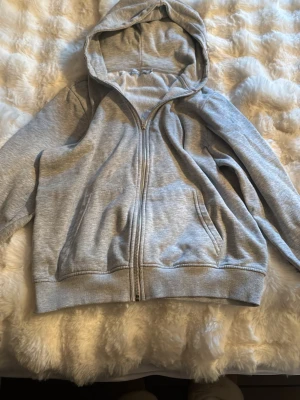 Ljusgrå zip-hoodie med huva - En stilren ljusgrå hoodie med dragkedja och huva. Hoodien har två fickor framtill och ribbade muddar vid ärmslut och nederkant. Perfekt för en avslappnad look och enkel att matcha med andra plagg.