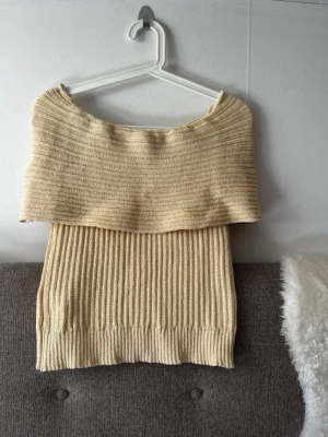 Beige off shoulder stickad topp - Trendig beige stickad topp med off shoulder-design och bred ribbstickning. Perfekt för lager-på-lager och ger en snygg siluett. Mjuk och stretchig, passar till många olika outfits.
