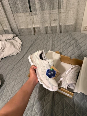 Asics gel nyc cream cloud grey 44 - Snygga vita sneakers från Asics med meshpaneler och syntetiska överdrag. Skorna har en chunky sula och klassisk snörning. Perfekta för dig som gillar sportig och clean stil. Diskret Asics-logga på sidan och tungan.