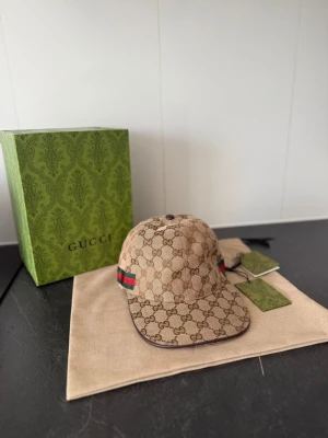 Gucci keps  - Säljer en beige keps från Gucci i GG Supreme-mönster med klassiska gröna och röda ränder på sidan. Helt ny, aldrig använd. Storlek M