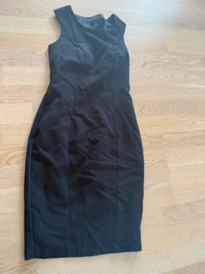 Svart ärmlös klänning från Selected Femme - Säljer en svart, figurnära klänning från Selected Femme. Klänningen är ärmlös med en klassisk, enkel design och markerad midja. Perfekt för dig som gillar stilrena plagg med snygg passform.