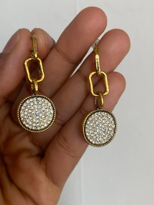 Guldiga örhängen med gnistrande stenar - Snygga örhängen i guldton med rund hängande detalj täckt av små gnistrande stenar. Örhängena har en modern länkdesign och ger en lyxig känsla. Perfekta för att lyfta din stil med lite extra bling.