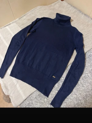 Mörkblå polotröja  - Snygg mörkblå polotröja med lång ärm och ribbade muddar. Tröjan har en klassisk, smal passform och är tillverkad i mjukt stickat material. 