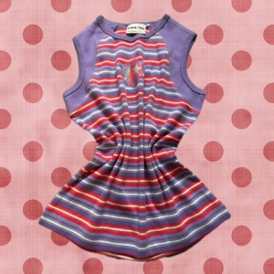 Randig croppad linnetopp i lila och rött - Superfin croppad linnetopp med lila, röda och vita ränder. Ärmlös modell med lila kanter och ett tryck med stjärna och hjärta framtill. Perfekt för dig som gillar färg och mönster!