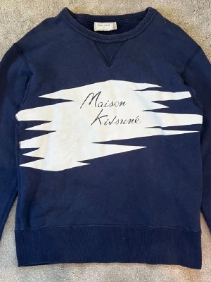 Blå sweatshirt Maison Kitsuné - Mörkblå sweatshirt från Maison Kitsuné med vit grafisk print och logga på bröstet. Nypris: 2500, kan tänka mig att pruta 😉