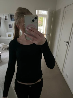 Svart långärmad topp med rund hals - En enkel och stilren svart långärmad topp med rundad halsringning. Toppens passform är kroppsnära och den är perfekt att matcha med jeans eller kjol. Materialet ser ut att vara mjukt och stretchigt, vilket gör den bekväm att bära.