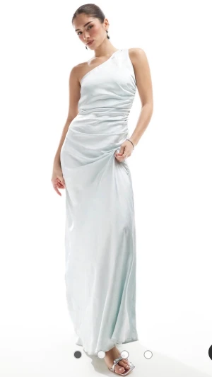 Blå oneshoulder långklänning - Ljusblå långklänning i oneshoulder-modell med slät, glansig yta (satin). Den är från six stories och köpt för ca 2500 kr förra året och är endast använd en gång på balen. I superfint skick förutom några små slitningar längst ned på baksidan (se bild). Den är i storlek 34 men passar mig som oftast har 36, jag är 170 och hade även klackar på bilderna.