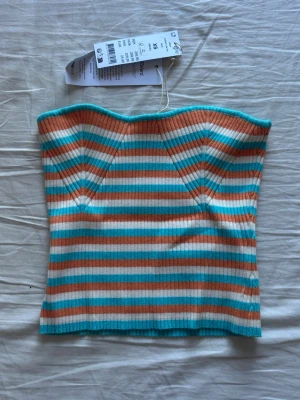 Randig ribbad tubtopp från Gina tricot  - Säljer en ribbad tubtopp från Gina tricot i sommarens färger. Toppen har horisontella ränder i turkos, orange och vitt, och är axelbandslös med bandeauform. 