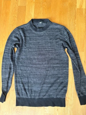 Mörkgrå stickad tröja från H&M - Mörkgrå stickad tröja från H&M med rund halsringning och ribbade muddar vid ärmslut och nederkant. Tröjan har en melerad look och är perfekt för lager-på-lager. Enkel och stilren design som passar till det mesta.