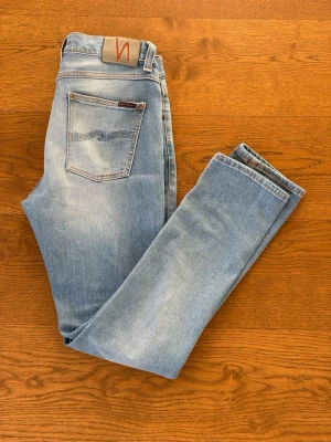 Ljusblå jeans från Nudie Jeans - Ett par rikgit snygga Nudie jeans modellen Lean Dean. Säljs pga att jag behöver pengar till AirPods Max annars hade jag inte sålt dem för att jag  tycker verkligen om färgen på dem. Köpt för ett tag sen men inte använt så mycket. Max 5ggr. Storlek 30/32. Hör av er vid frågor och bud!