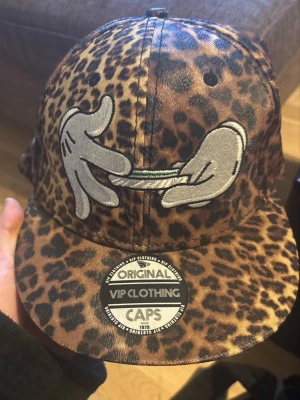 Leopardmönstrad keps från VIP Clothing - Säljer en leopardmönstrad keps från VIP Clothing med broderad design av tecknade händer som rullar en cigarett på framsidan. Kepsen har platt skärm och sticker ut med sitt djurmönster och coola brodyr. Perfekt för dig som vill ha en unik och trendig accessoar.