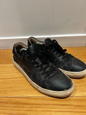 Gianni Feraud Sneakers *42* - Klassiska svarta sneakers i läder med vita sulor och svarta skosnören. Modellen är låg och har en enkel, stilren design som passar till det mesta. Insidan är ljusbrun och sulan har en diskret struktur. Perfekta för dig som gillar en clean look.