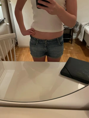 Blå lågmidjade jeansshorts från Levi's - Säljer ett par klassiska blå jeansshorts från Levi's med fem fickor och knappgylf. Shortsen har låg midja och en normal passform. Slitningarna som är på shortsen var där från början.Det står för 14 åringar på dem men skulle säga att de är i storlek 32-34 eller xs. Välanvända shorts som jag personligen älskar men är tyvärr lite för små. Perfekta till sommaren och lätta att matcha med massa kläder💕