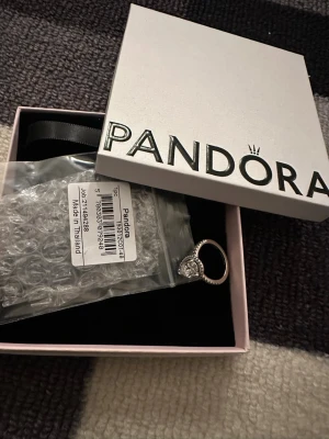 Pandora silverring med droppformad sten - Snygg silverring från Pandora med en stor, droppformad klar sten i mitten och mindre stenar runt om. Ringen har en glittrande design och levereras i originalask. Perfekt för dig som gillar statement-smycken. Storlek 14,mm