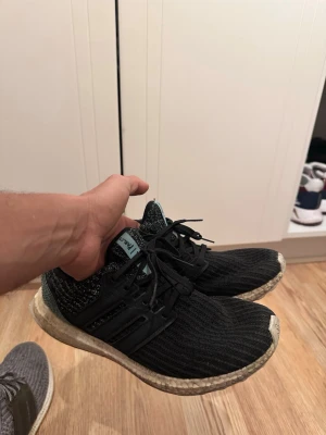 Svarta Adidas Ultraboost sneakers - Svarta Adidas Ultraboost sneakers med stickad ovandel och svarta detaljer. Skorna har en vit Boost-sula och klassiska tre ränder på sidan. Lätta och bekväma med snörning och låg profil. Perfekta för en sportig och stilren look.