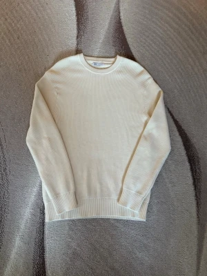 Krämvit stickad tröja från Zara  - Snygg krämvit stickad tröja från Zara med rund halsringning och ribbade muddar vid ärmslut och nederkant. Tröjan är i ett mjukt, tunt stickat material och har en klassisk, rak passform. Perfekt för lager-på-lager-stil.