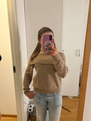 Beige off shoulder stickad tröja - Säljer en beige stickad tröja med bred off shoulder-krage och ribbstickade muddar. Tröjan är mjuk och har en avslappnad passform, perfekt för att skapa en chill look.