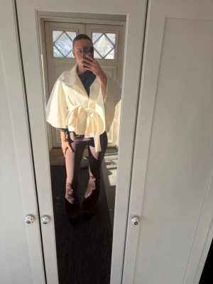 Vit cape-kappa med knytskärp - Säljer en elegant vit cape-kappa med bred krage och knytskärp i midjan. Kappan har en luftig och flowy passform med korta ärmar och är perfekt för att skapa en stilren look. Materialet ser ut att vara mjukt och bekvämt, troligen ullblandning.