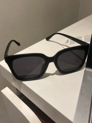 Svarta cat eye solglasögon - Snygga svarta solglasögon i cat eye-modell med breda bågar. Perfekta för att ge en cool och trendig look. Glasögonen har mörka linser och en stilren design som passar till de flesta outfits.