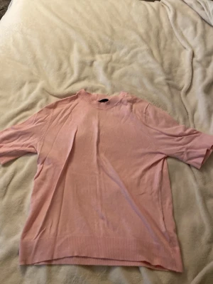 Ljusrosa tröja från 157, kort ärm - Ljusrosa tröja från 157 med korta ärmar och ribbade detaljer vid hals, ärmslut och nederkant. Enkel och stilren design som passar perfekt till jeans eller kjol. Mjuk och skön kvalitet, perfekt för vår och sommar.