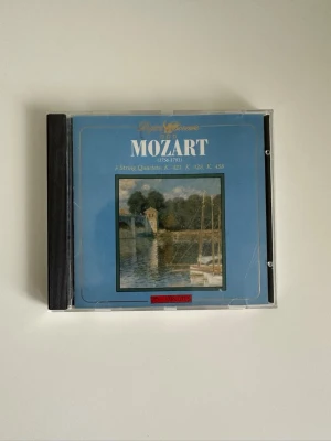 Mozart CD - 3 String Quartets - CD med klassisk musik av Mozart, innehåller tre stråkkvartetter (K. 421, K. 428, K. 458). Omslaget är blått med konstmotiv och plastfodral. Perfekt för dig som gillar klassisk musik och vill ha något snyggt till samlingen.