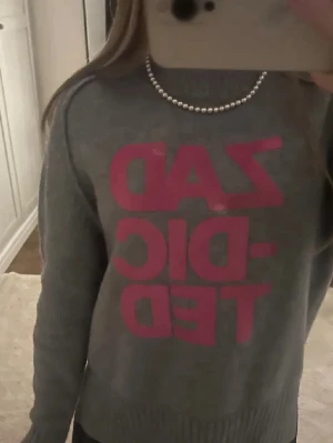 Grå stickad tröja med rosa tryck - Så snygg stickad tröja från Zadig! Lite av den rosa texten har försvunnit, men annars är det inga större problem.💓(skriv gärna vid fler frågor)